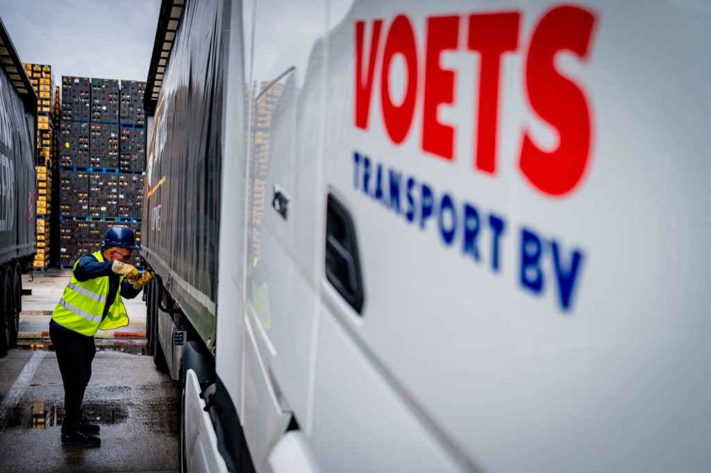 Medewerker bij een Voets Transport oplegger met stapels drankkratten op de achtergrond