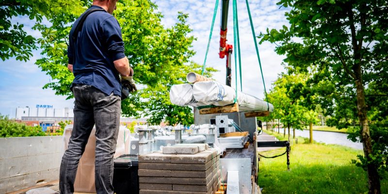Chauffeur lost pallets bouwmateriaal met de kraan van de oplegger